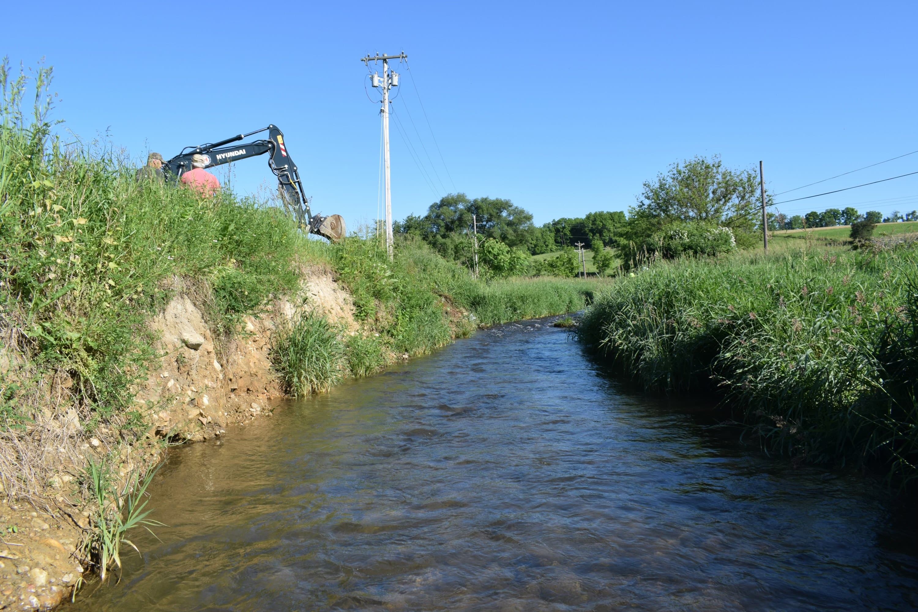 Hyundai excavator perched on the edge of a high eroded streambank