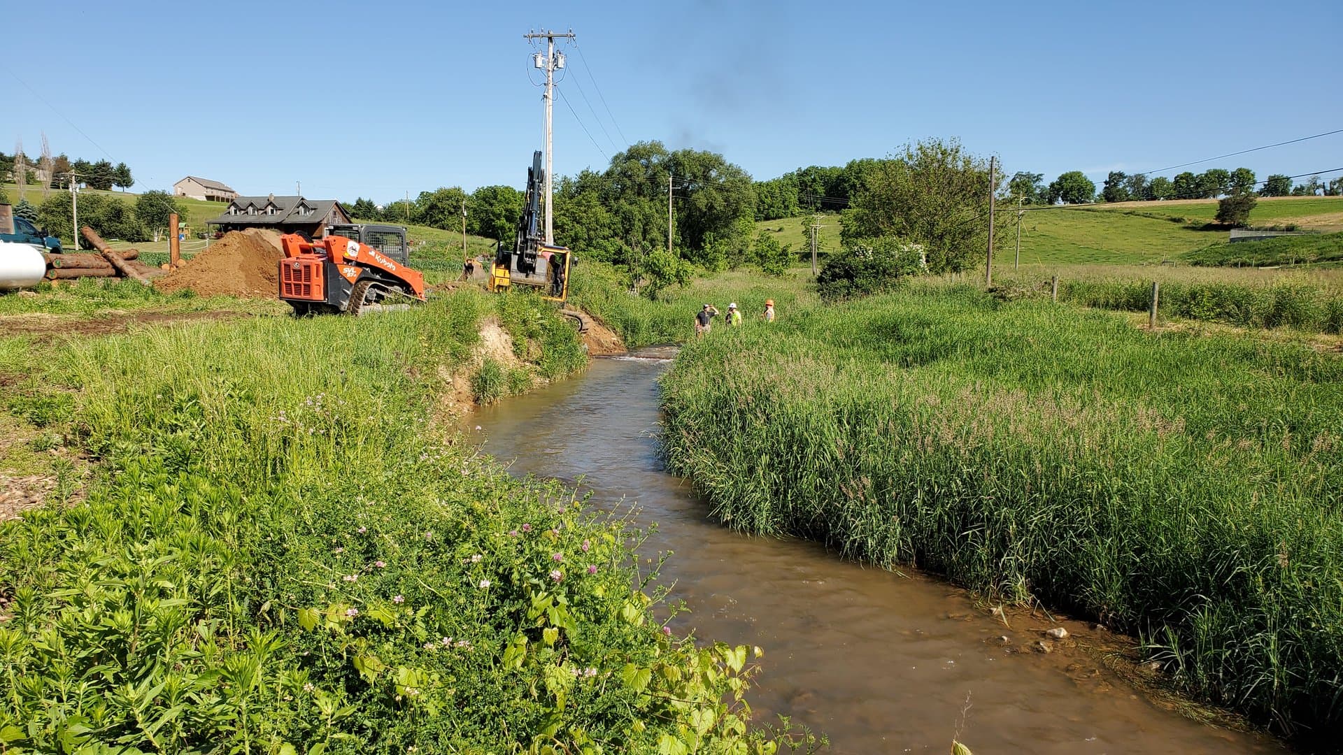Kubota skid steer and drill rig staged beside the stream for bank stabilization