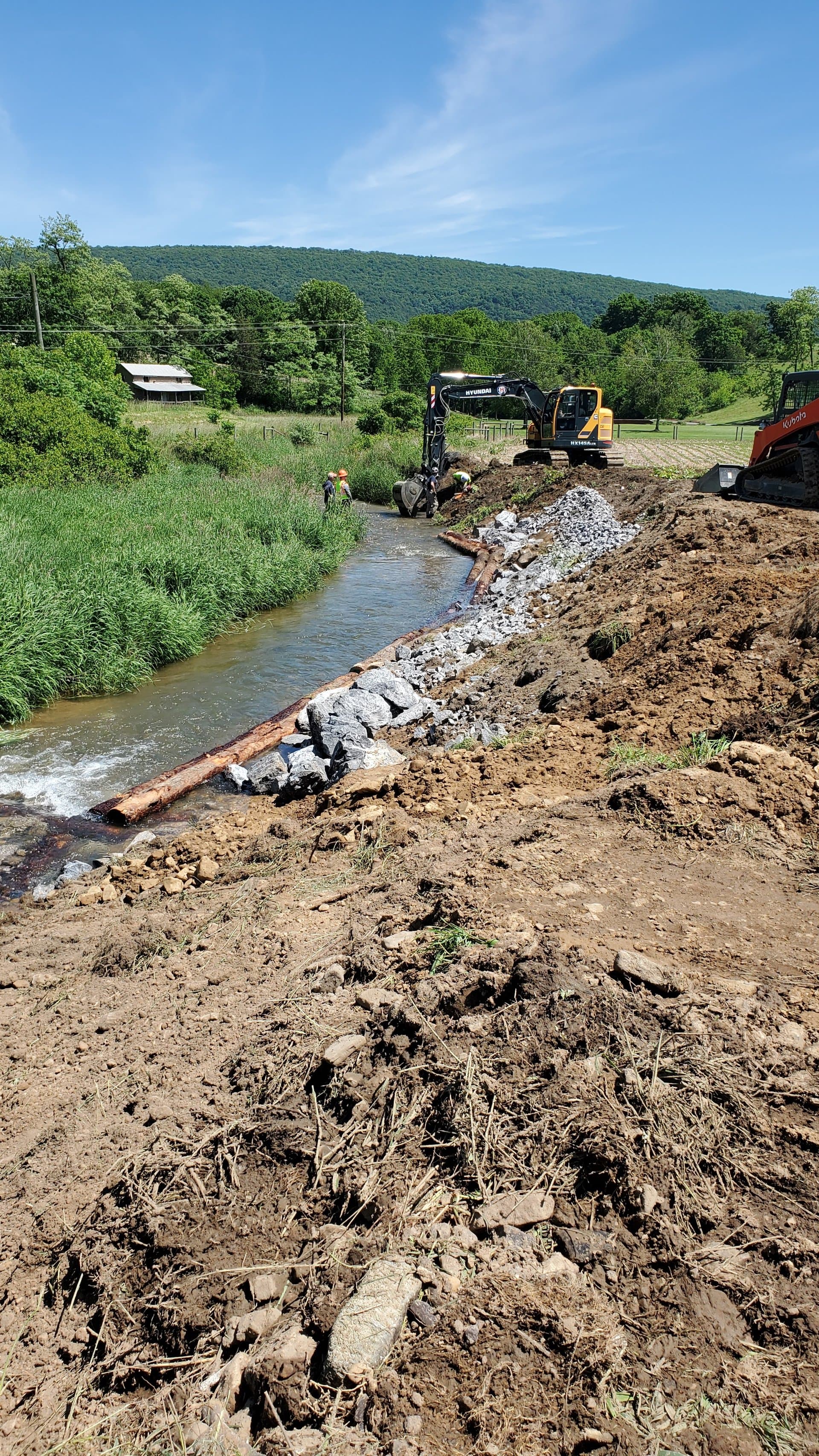Excavator and skid steer building a stone deflector on the streambank